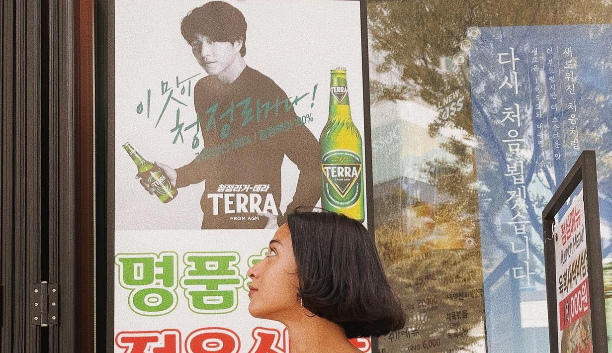 <p>Yang ini, dia foto bareng poster Gong Yoo untuk iklan sebuah minuman. Ibu satu anak ini tampak serius melihat ketampanan aktor kesayangannya. (Foto: Instagram/ putrimarino)</p>