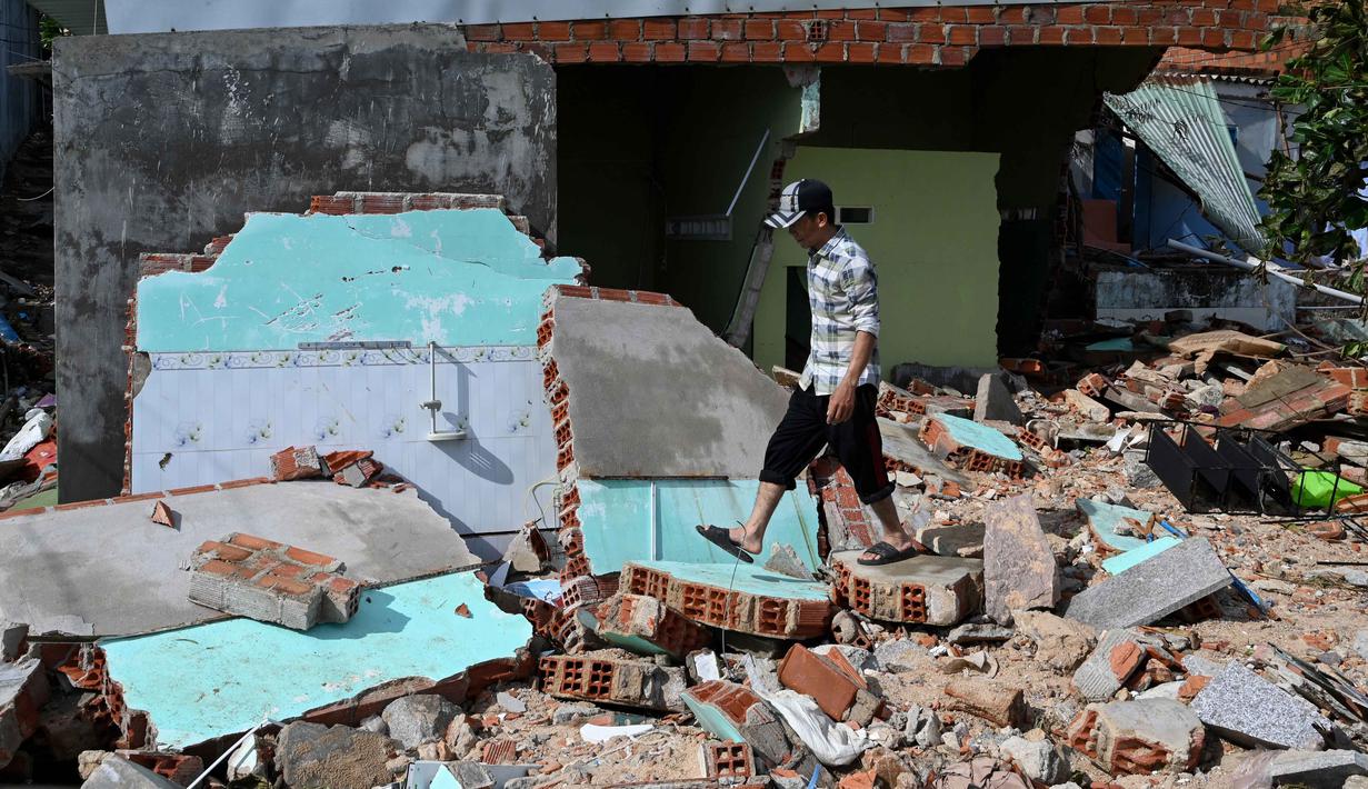 Badan Penanggulangan Bencana Vietnam menyebut sekitar 2.800 rumah mengalami kerusakan dan lebih dari 1,3 juta penduduk kehilangan akses listrik. Tampak dalam foto, seorang warga berjalan di atas puing-puing bangunan yang hancur akibat angin kencang di desa nelayan Nhon Hai dekat Quy Nhon, Provinsi Gia Lai, Vietnam Tengah, pada Jumat 7 November 2025. (NHAC NGUYEN/AFP)