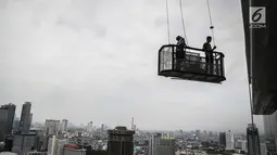 Pekerja naik gondola tanpa helm keselamatan beraktivitas di gedung bertingkat di Jakarta, Rabu (15/11). Banyak kejadian kecelakaan kerja di ketinggian disebabkan karena mahalnya peralatan pengaman pribadi yang ada di pasaran. (Liputan6.com/Faizal Fanani)