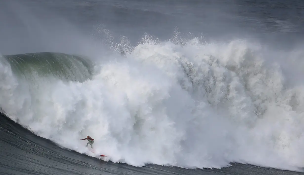 Aksi seorang peselancar berdiri di papannya saat ombak besar menggulung di Praia do Norte di Nazare, Portugal (19/11). Selancar atau surfing adalah salah satu jenis olahraga ekstrim yang bisa dijadikan latihan kardiovaskular. (Reuters/Rafael Marchante)