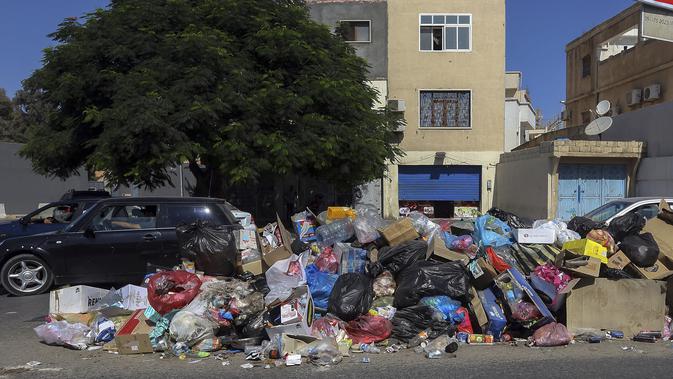 Mobil parkir di dekat tumpukan sampah di sepanjang sisi jalan di Tripoli, ibukota Libya (30/9/2019). Sampah yang berserakan di jalan tersebut menambah cobaan sehari-hari bagi penduduk ibukota yang kehidupannya telah diselingi kekurangan bahan bakar, listrik, dan air. (AFP Photo/Mahmud Turkia)