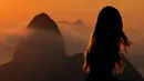 Seorang turis berpose saat matahari terbit dengan latar belakang gunung Sugarloaf di Bukit Corcovado di Rio de Janeiro, Brasil, pada 24 Maret 2023. (Photo by Carl DE SOUZA / AFP)