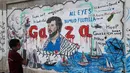 Seorang anak laki-laki Palestina melihat mural yang menggambarkan pencegatan kapal-kapal yang berpartisipasi dalam Armada Sumud Global, sebuah misi bantuan kemanusiaan yang dipimpin sipil ke Gaza melalui laut, di Nuseirat, Jalur Gaza Tengah pada 19 Mei 2026. (Eyad Baba/AFP)
