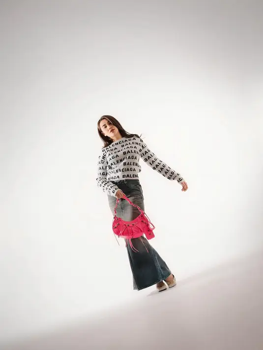 Aaliyah Massaid tampil gaya dengan one brand outfit. Ia mengenakan atasan lengan panjang bermotif logo brand dengan rok denim panjang, dan membawa handbag pink yang mencolok. [Foto: Instagram/aaliyah.massaid]