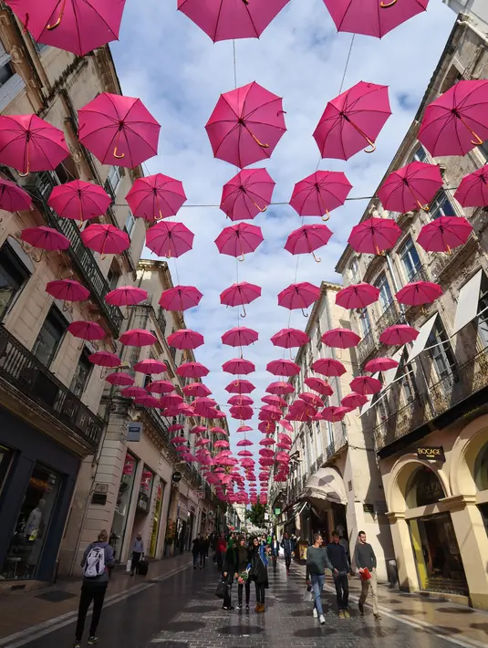 Pejalan kaki melintasi ratusan payung pink yang digantung sebagai tanda dukungan atas kewaspadaan bahaya kanker payudara di Montpellier, Prancis, Selasa (9/10). Bulan Oktober, ditetapkan sebagai bulan kewaspadaan atas kanker payudara. (AFP/PASCAL GUYOT)