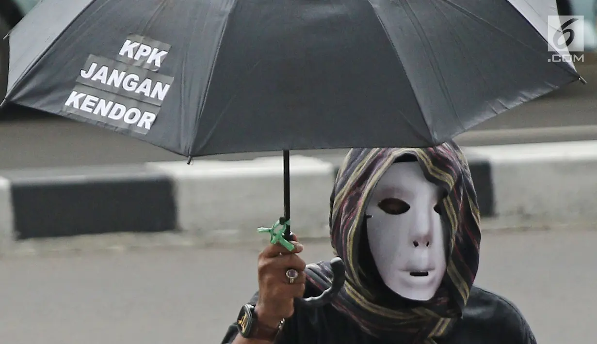 Seorang demonstran menggunakan topeng dan payung saat berunjuk rasa di depan Gedung KPK, Jakarta, Jumat (9/3). Demonstran mendesak KPK menahan Gubernur Jambi Zumi Zola karena sudah ditetapkan sebagai tersangka suap. (Liputan6.com/Herman Zakharia)
