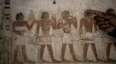 Seorang arkeolog Mesir menunjuk ke sebuah lukisan berwarna yang menunjukkan persembahan korban di sebuah makam yang baru-baru ini ditemukan yang dikatakan milik seorang pejabat tinggi Dinasti kelima bernama "Ne Hesut Ba" (2400 SM), di situs Step Pyramid of Djoser di Saqqara, 24 kilometer (15 mil) barat daya Kairo, Sabtu, 27 Mei 2023. (AP Photo/Amr Nabil)