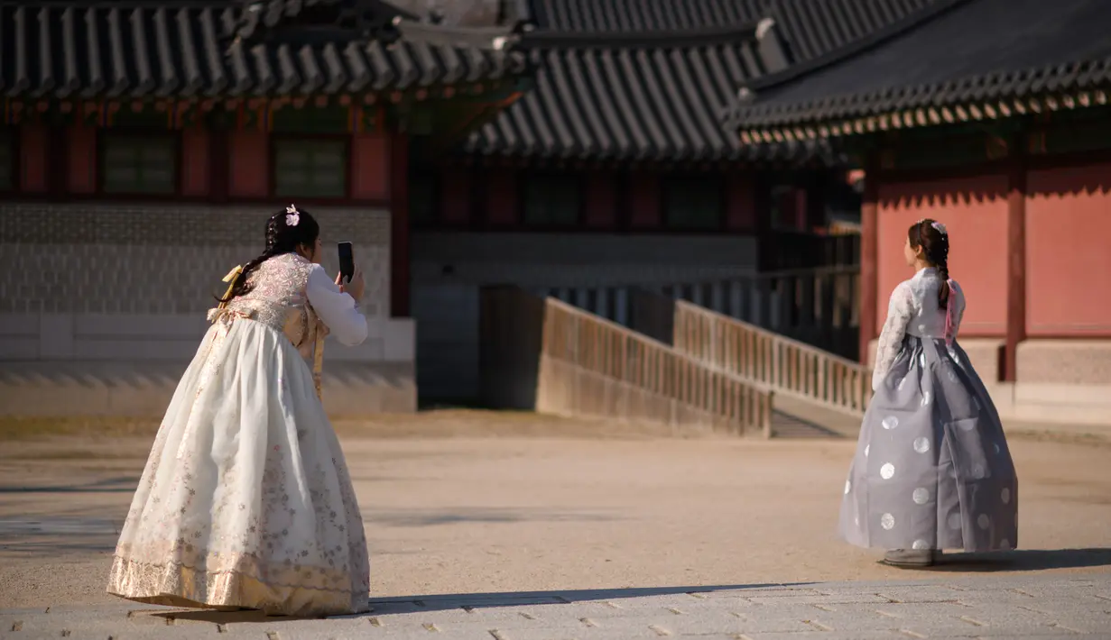 Pengunjung mengenakan pakaian tradisional Hanbok mengambil foto di istana Changdeokgung di Seoul , Korea Selatan (2/4). Korea Selatan sedang bersiap untuk meluncurkan jaringan seluler 5G pertama di dunia pada 5 April. (AFP Photo/Ed Jones)