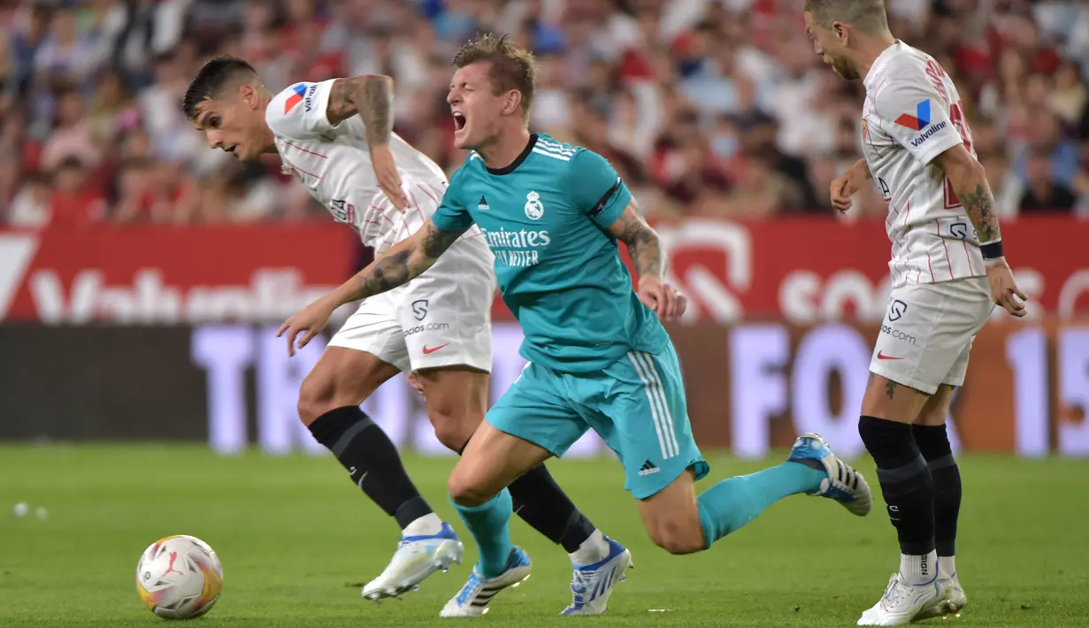 Gelandang Real Madrid Toni Kroos (tengah) terjatuh saat melawan Sevilla pada lanjutan Liga Spanyol di stadion Ramon Sanchez Pizjuan, Senin (18/4/2022) dini hari WIB. Real Madrid sukses menaklukkan Sevilla 3-2. (CRISTINA QUICLER / AFP)