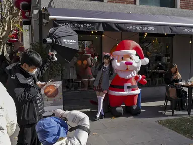 Seorang gadis China berpose untuk pemotretan dengan sosok Sinterklas yang dipajang di luar restoran yang dihias musim Natal di Shanghai pada 17 Desember 2023. (AP Photo/Wayne Zhang)