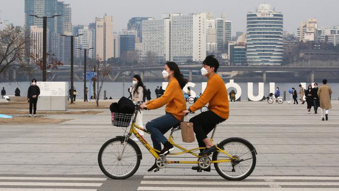 Sepasang kekasih mengenakan masker saat bersepeda  di sebuah taman di Seoul, Korea Selatan, 7 Maret 2020. Hingga Kamis (12/3/2020) pagi, jumlah kasus virus corona COVID-19 di Korea Selatan sebanyak 7.755 orang terinfeksi, 60 meninggal, dan 288 sembuh. (AP Photo/Ahn Young-joon)
