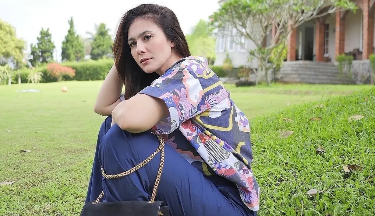Duduk di hamparan rumput hijau, Wulan Guritno terlihat mengenakan blouse bermotif dengan celana panjang bernuansa biru. Ia juga terlihat melilitkan Saint Laurent Kate Medium Reversible Chain Bag (in Shiny Leather & Suede) di kakinya, yang harganya diperkirakan sekitar Rp25 jutaan. Foto: Instagram.