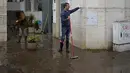 Seorang pria yang menyapu air dari sebuah gedung menunjukkan ketinggian yang dicapai air saat jalan dibanjiri semalaman di Alges, tepat di luar Lisbon, Selasa (13/12/2022). Badai Atlantik menghantam semenanjung Iberia, meninggalkan jejak kehancuran pada Selasa, terutama di Ibu kota Portugal,  Lisbon, sebelum pindah ke timur ke Spanyol.  (AP Photo/Armando Franca)
