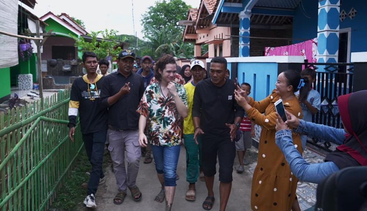 Saat melewati jalan kecil, adik Al Ghazali itu tampak menebar senyum kepada warga yang mengarahkan kamera padanya. Sambil dikawal oleh dua orang berbaju hitam, Dul berjalan dengan santai sambil menyapa ibu-ibu yang senang bertemu dengannya. Dalam kesempatan tersebut, Dul memakai kemeja motif bunga dan celana jeans. (Liputan6.com/IG/@duljaelani)