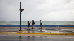 Sekelompok wisatawan berjalan di dekat laut sebelum kedatangan Badai Tropis Fiona di San Juan, Puerto Rico, Sabtu (17/9/2022). Setelah dari Puerto Rico, Fiona diproyeksikan melintasi Republik Dominika pada Senin mendatang dengan ancaman hujan deras yang berpotensi memicu banjir bandang atau longsor. (AP Photo/Alejandro Granadillo)