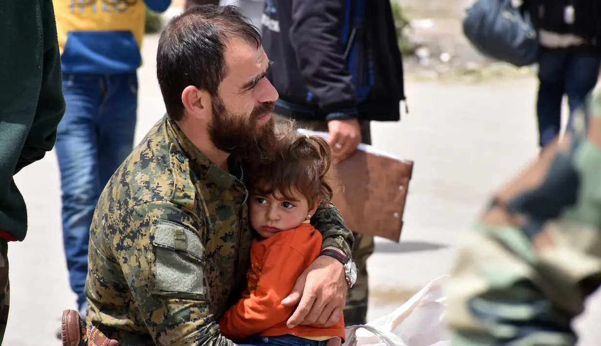 Seorang lelaki memeluk bocah saat berada di sebuah tempat penampungan sementara di Jibrin di pinggiran timur Aleppo, Jumat (21/4). Pengungsi adalah warga dari kota Fuaa dan Kafraya. (AFP PHOTO / George OURFALIAN)