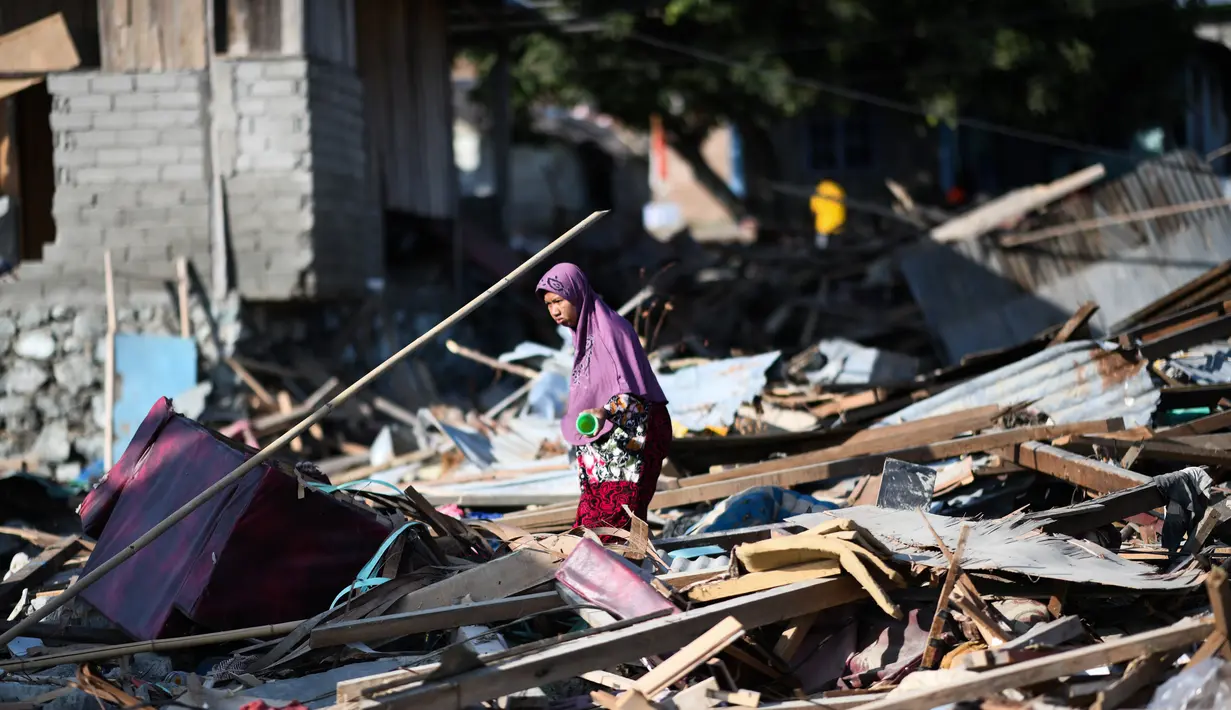 Seorang wanita mencari barang-barang yang tersisa di antara puing rumah akibat gempa dan tsunami di Donggala, Sulawesi Tengah, Jumat (5/10). Gempa bumi berkekuatan 7,4 skala richter melanda Palu dan Donggala pada 28 September 2018 lalu. (AFP/Jewel SAMAD)