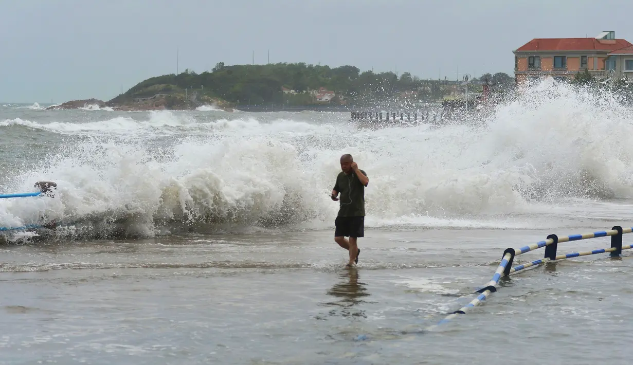 Seorang pria berjalan saat ombak besar yang disebabkan Topan Yagi di sepanjang pantai laut di Qingdao di provinsi Shandong timur China (13/8). Menurut Kantor Berita Xinhua, Topan Yagi memiliki kecepatan hingga 102 kilometer per jam. (AFP Photo)