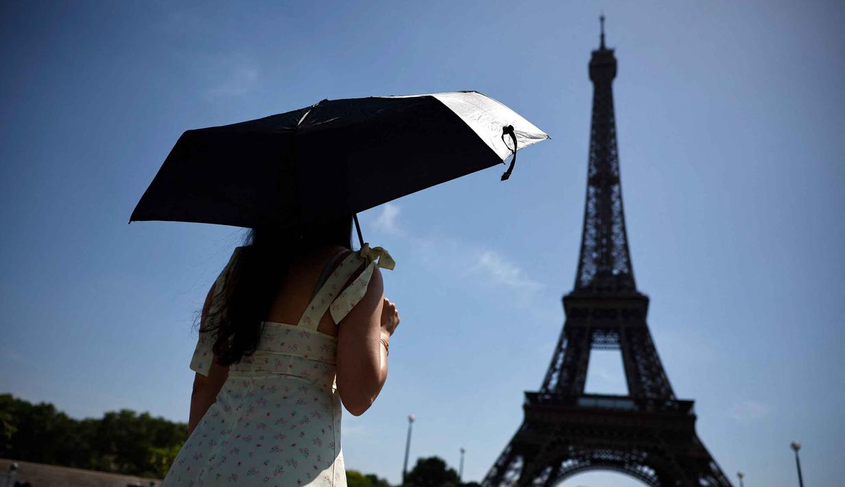 Seseorang berlindung di bawah payung saat berjalan menuju Menara Eiffel di Paris ketika gelombang panas yang memecahkan rekor melanda sebagian besar Eropa Barat pada Kamis 28 Mei 2026. (SIMON WOHLFAHRT/AFP)