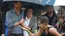 Pangeran Harry dan Meghan Markle berlindung di bawah payung menyaksikan tarian aborigin saat piknik di Victoria Park, Dubbo, Australia, Rabu (17/10). Ini adalah hari kedua Harry dan Markle dalam kunjungannya ke Australia. (Ian Vogler/Pool via AP)