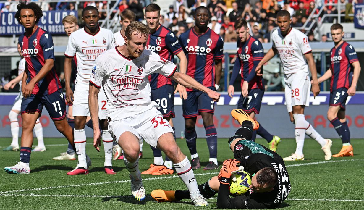 Pemain AC Milan, Tommaso Pobega (tengah kiri) berusaha mencetak gol ke gawang Bologna yang dijaga Lukasz Skorupski pada laga lanjutan Liga Italia 2022/2023 di Renato-Dall'Ara Stadium, Bologna, Minggu (16/04/2023) WIB. Laga berakhir dengan skor imbang 1-1. (AFP/Alberto Pizzoli)
