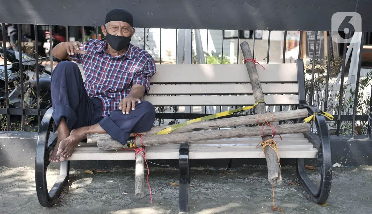 Warga nekat duduk di bangku trotoar yang disegel garis pembatas dan ditutupi bambu di kawasan Rawamangun, Jakarta, Minggu (3/5/2020). Bangku trotoar di sepanjang jalan Rawamangun disegel untuk mencegah kerumunan warga sebagai upaya memutus rantai penyebaran COVID-19. (merdeka.com/Iqbal S. Nugroho)