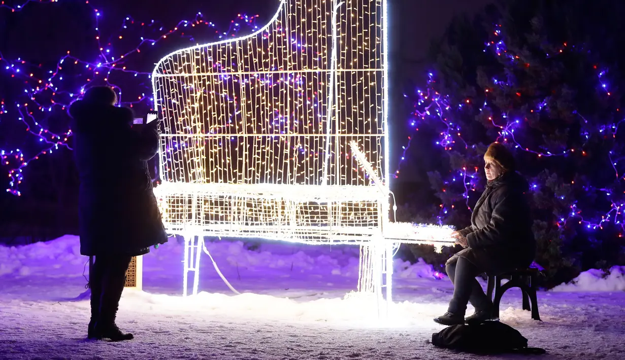 Seorang wanita berpose disamping cahaya lampu berbentuk piaono di sebuah taman di Minsk, Belarus (28/12). Setelah matahari terbenam, orang-orang berdatangan untuk menikmati pameran cahaya lampu yang dipasang di seluruh taman. (AP Photo/Grits Sergei)
