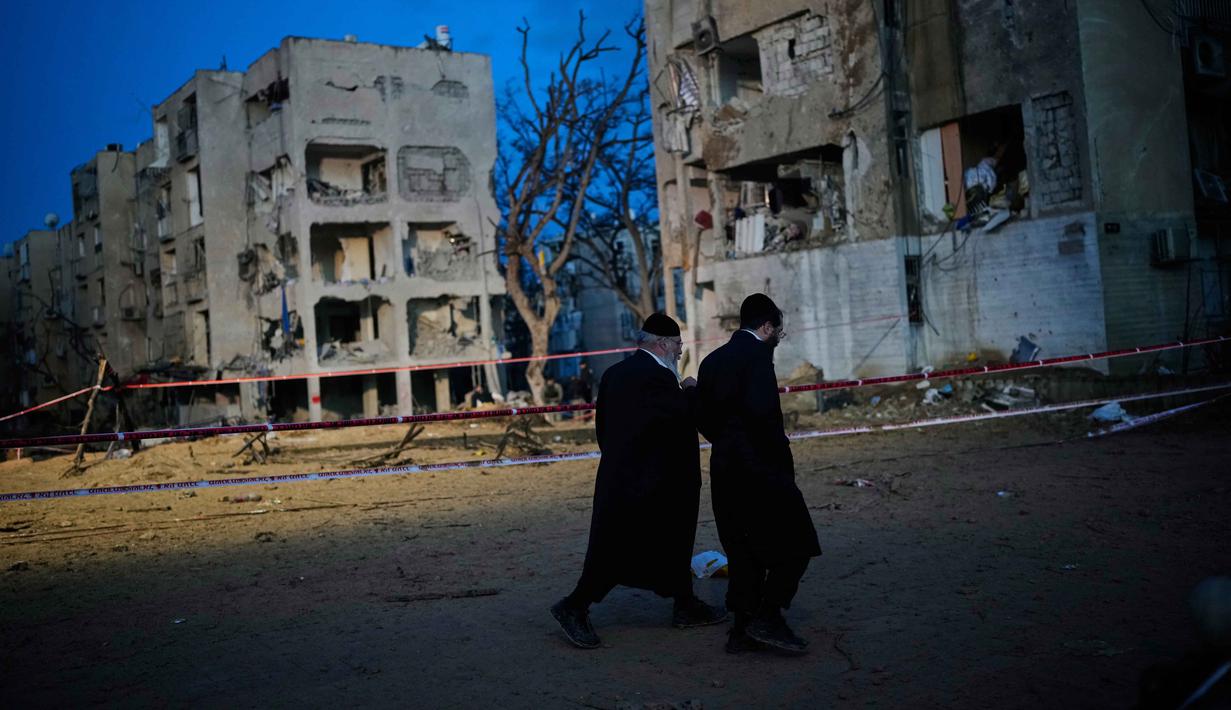 Otoritas keamanan Israel mengimbau warga tetap waspada, mematuhi instruksi darurat, serta segera menuju tempat perlindungan saat sirene peringatan berbunyi. Tampak dalam foto, warga melihat bangunan tempat tinggal yang rusak parah akibat serangan rudal Iran di Arad, Israel Selatan, Minggu, 22 Maret 2026. (AP Photo/Ohad Zwigenberg)