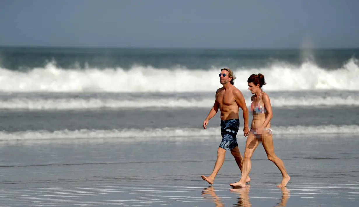 Dua turis berjalan saat berlibur di Pantai Kuta di Denpasar, Bali (27/9). Meski berjarak sekitar 75 kilometer dari pusat gunung berapi, para turis masih banyak yang mendatangi Pantai Kuta di Bali. (AFP Photo/Sony Tumbelaka)