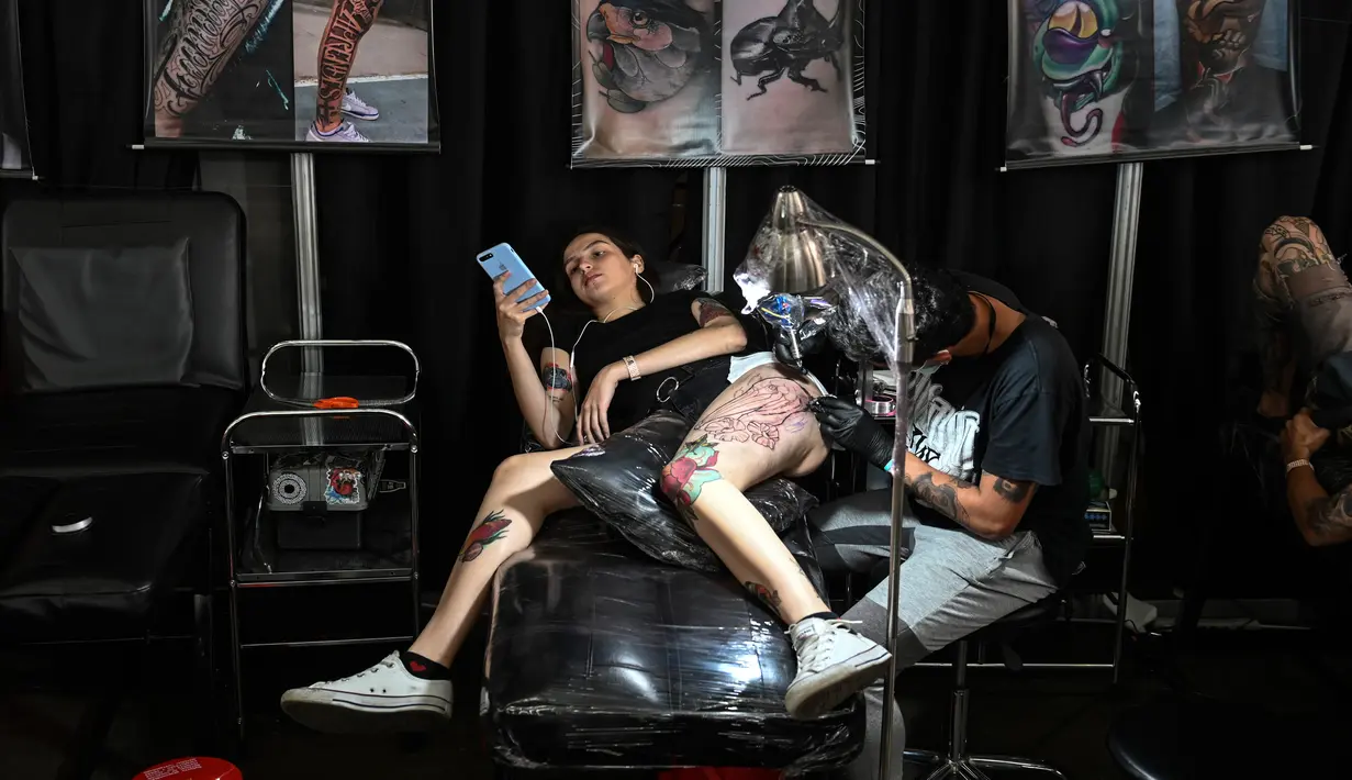 Seorang wanita bermain ponsel saat membuat tato dikakinya selama Expotattoo Colombia 2019 di Medellin, departemen Antioquia (2/6/2019). Para penggila tato antusias untuk mentato tubuhnya di festival tato terbesar di negara tersebut. (AFP Photo/Joaquim Sarmiento)