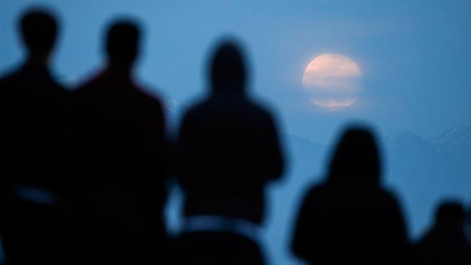 Orang-orang menyaksikan fenomena gerhana bulan total atau supermoon dengan latar belakang pusat kota Los Angeles dari Kenneth Hahn Park, Minggu (20/1). Supermoon akhir pekan ini adalah yang pertama terjadi pada tahun 2019 ini. (AP/Ringo H.W. Chiu)
