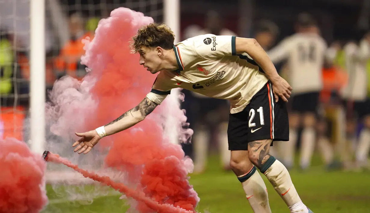 Pemain Liverpool Kostas Tsimikas membersihkan suar yang dilempar pendukung usai rekan setimnya Diogo Jota mencetak gol ke gawang Nottingham Forest pada pertandingan sepak bola perempat final Piala FA di City Ground, Nottingham, Inggris, Minggu (20/3/2022). Liverpool menang 1-0. (AP Photo/Jon Super)