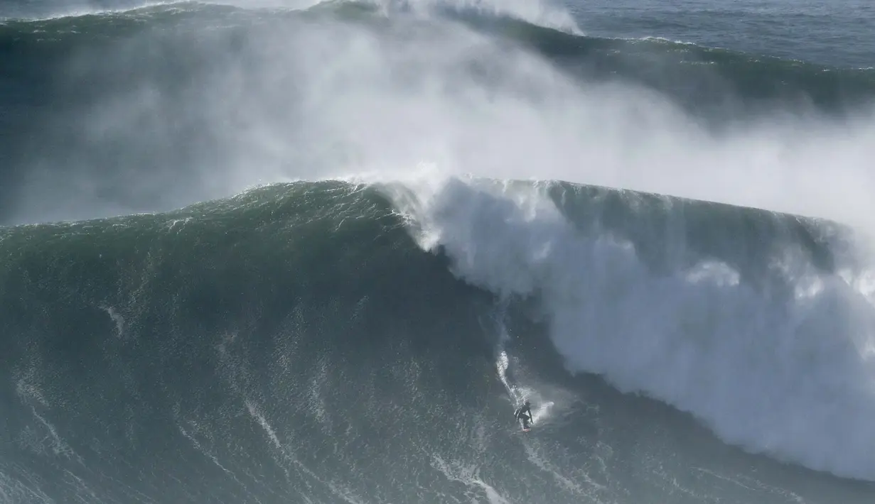 Seorang peselancar turun ombak selama sesi selancar derek di Praia do Norte atau Pantai Utara di Nazare, Portugal (29/10/2020). Gelombang besar, yang ditimbulkan oleh Badai Epsilon di Atlantik Utara, mencapai Portugis pantai barat menarik peselancar ombak besar ke Nazare. (AP Photo/Pedro Rocha)