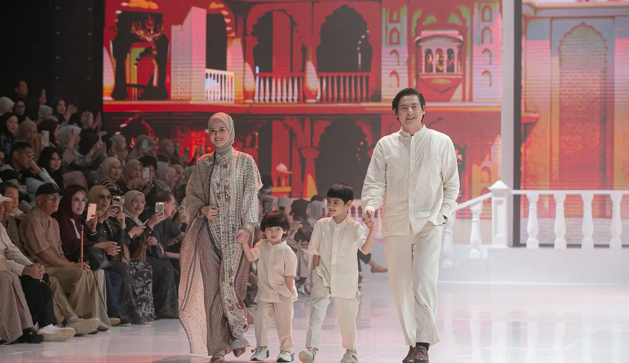 Cut Ratu Meyriska tampil bersama sang suami, Roger Danuarta, serta dua anak mereka. Ia mengenakan busana bernuansa soft dengan lapisan outer tipis yang memberi efek ringan dan flowy. Detail motif kecil yang tersebar di seluruh permukaan kain memberi karakter lembut, sementara tampilan keluarga yang serasi dalam palet warna senada menghadirkan potret runway yang terasa personal, hangat, dan emosional. [Dok/Shi by Shireen & Zaskia Sungkar].