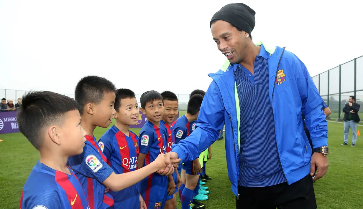 Mantan pemain Barcelona, Ronaldinho, menyalami anak-anak saat peluncuran akademi sepak bola Barcelona di China, Jumat (24/2/2017). (AFP/Handout)