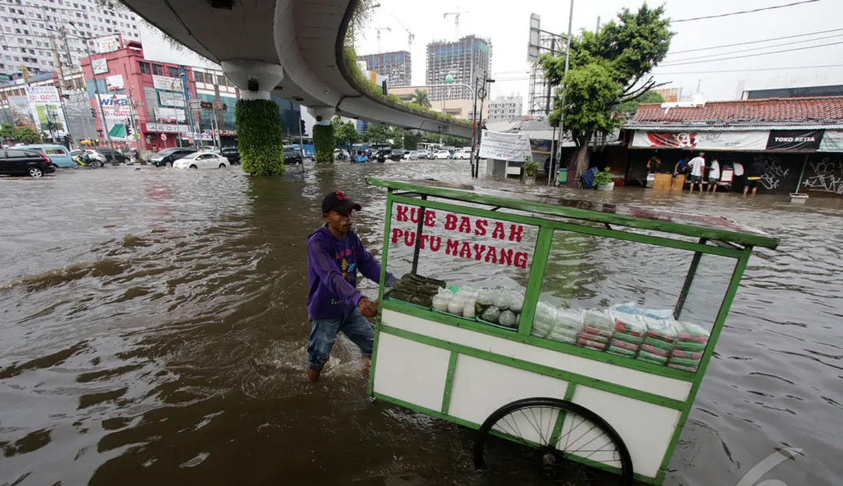 Seorang pedagang terlihat mendorong gerobaknya melewati genangan air di Jalan Matraman, Jakarta, Sabtu (27/12/2014). (Liputan6.com/Miftahul Hayat)