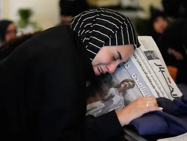 Zainab, saudara perempuan jurnalis Lebanon Amal Khalil yang tewas dalam serangan udara Israel pada Rabu 22 April 2026, memegang koran yang menampilkan potret saudara perempuannya, saat ia berduka di atas peti matinya di desa Baysariyeh, Lebanon Selatan, Kamis 23 April 2026. Jurnalis surat kabar Al-Akhbar, Amal Khalil, ditemukan meninggal dunia imbas serangan udara Israel di Kota al-Tayri, Lebanon Selatan pada Rabu 22 April 2026. (AP Photo/Mohammed Zaatari)