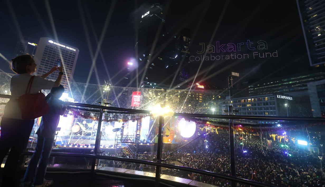 Warga mengabadikan pertunjukan drone saat perayaan malam pergantian tahun di kawasan Bundaran Hotel Indonesia, Jakarta, Rabu (31/12/2025). Untuk memeriahkan malam pergantian tahun tanpa kembang api, puluhan drone diterbangkan dan menghiasi langit Jakarta. (Kapanlagi.com/Budy Santoso)