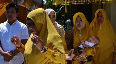 Tokoh adat dan agama menggendong bayi pada ritual 'peutron tanoh aneuk' (turun tanah anak) di Banda Aceh, Aceh, Senin (15/7/2019). Ritual turun tanah anak yang telah menjadi tradisi sakral bagi masyarakat Aceh yang dilaksanakan pada saat bayi berusia 44 hari. (CHAIDEER MAHYUDDIN / AFP)