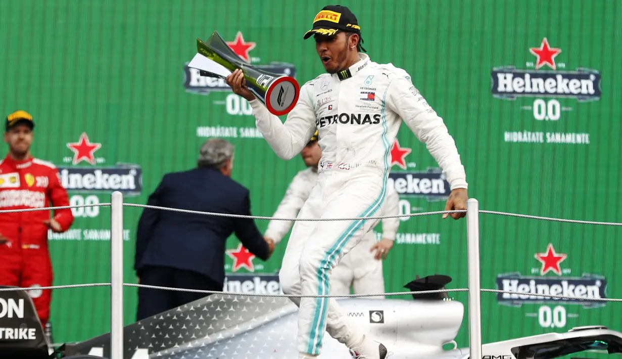 Pembalap Mercedes Lewis Hamilton berselebrasi membawa pialanya setelah berhasil menjuarai balapan GP Meksiko di Autodromo Hermanos Rodriguez, Mexico City (28/10/2019). Hamilton unggul 74 poin atas Bottas di posisi kedua klasemen dengan 289 poin. (AP Photo/Eduardo Verdugo)