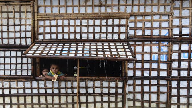Anak-anak pengungsi Rohingya melihat keluar dari rumah saat hujan lebat di kamp pengungsi Kutupalong di Ukhia 12/9/2019). Kamp ini adalah salah satu dari dua kamp pengungsi yang dikelola pemerintah di Cox's Bazar, kamp yang satunya lagi adalah kamp pengungsi Nayapara. (AFP Photo/Munir Uz Zaman)
