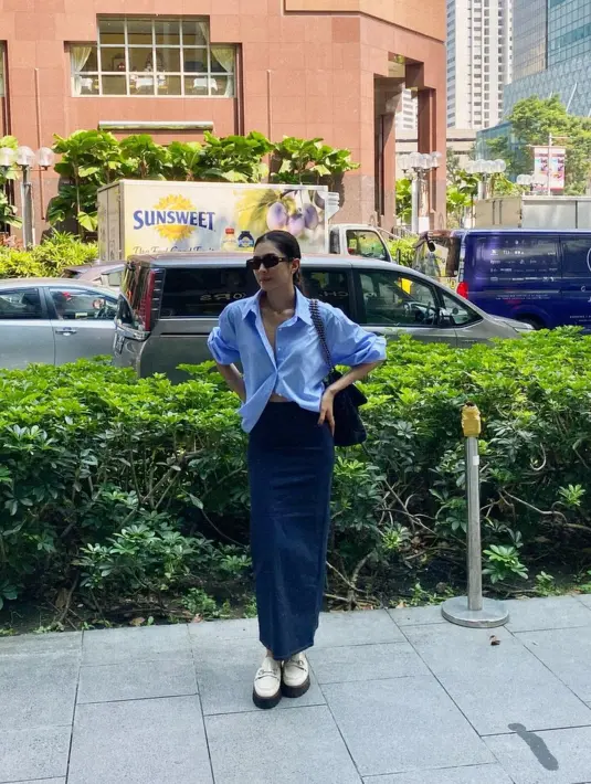 Outfit liburan yang simple chic ala Mikha Tambayong. Ia mengenakan kemeja biru lengan panjang yang dilipat dan ia padukan dengan rok biru panjang, serta sunglasses dan sepatu putih. [Foto: Instagram/miktambayong]