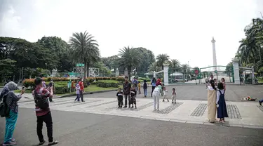 Warga berfoto di halaman luar Monumen Nasional (Monas) Jakarta, Kamis (5/5/2022). Meski kawasan Monas masih ditutup sejak awal pandemi COVID-19 pada Maret 2020 lalu namun tidak menyurutkan minat warga untuk bisa berwisata yaitu dengan memanfaatkan kawasan luar monumen tersebut. (Liputan6.com/Faizal Fanani)