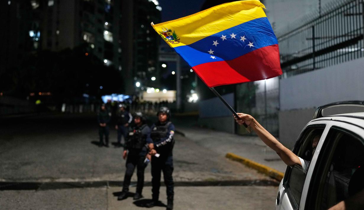 Percepatan pembebasan tahanan ini terjadi setelah penangkapan mantan Presiden Nicolas Maduro oleh militer Amerika Serikat pada 3 Januari 2026 lalu. Tampak dalam foto, Seorang pendukung oposisi mengibarkan bendera Venezuela dari sebuah kendaraan yang lewat di dekat El Helicoide, markas besar dinas intelijen dan pusat penahanan, setelah beberapa tahanan politik dibebaskan dari tahanan, Caracas, Venezuela, Minggu 8 Februari 2026. (AP Photo/Ariana Cubillos)