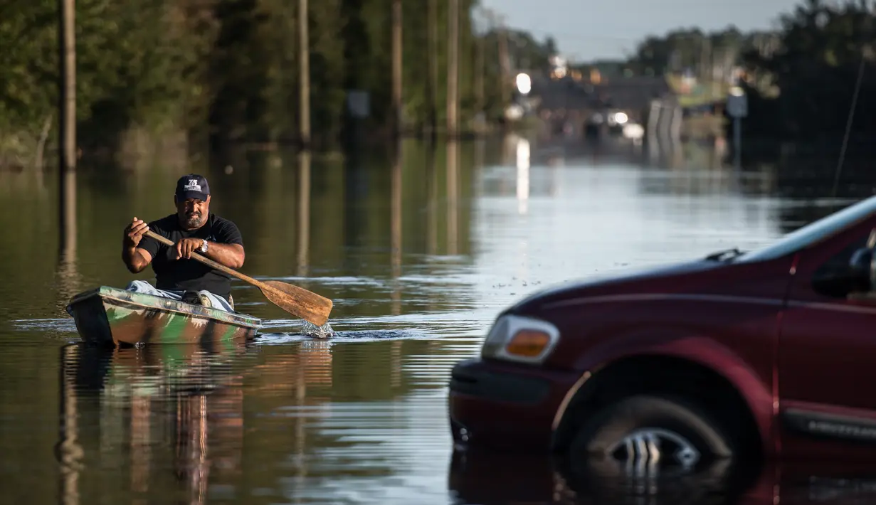 Eric Locklear mendayung kano melewati mobil yang terendam banjir di Lumberton, Carolina Utara, AS, 12 Oktober 2016. Banjir akibat badai Matthew tersebut merendam kota berpenduduk 21.000 orang itu. (Sean Rayford/Getty Images/AFP)
