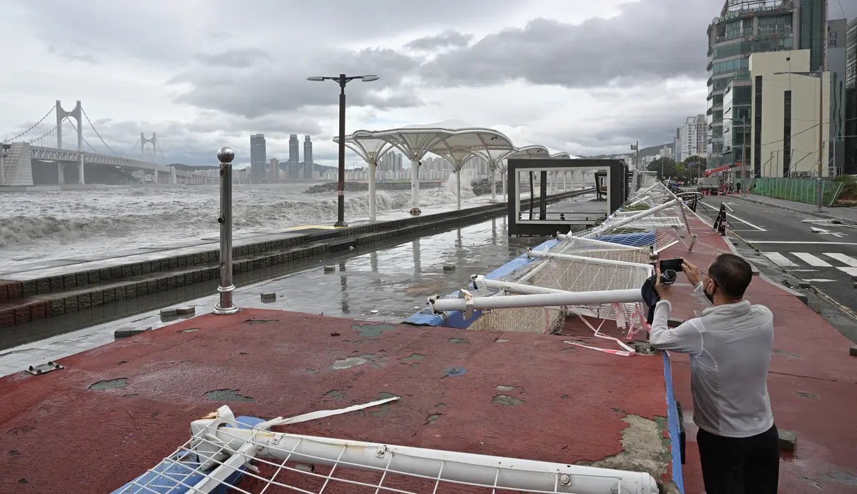 Seorang pria berdiri di samping pagar yang rusak saat mengambil foto ombak, setelah Topan Hinnamnor melewati Busan, Korea Selatan (6/9/2022). (AFP/Anthony Wallace)