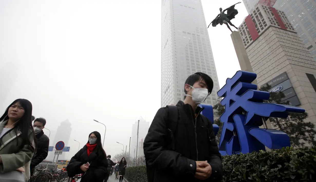 Sejumlah warga berjalan mengenakan masker saat beraktivitas di distrik Beijing pusat bisnis, Tiongkok, (21/12). Kabut asap akibat polusi udara yang melanda sebagian kota-kota di Tiongkok membuat warga beraktivitas mengunakan masker. (Reuters/Jason Lee)