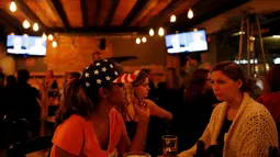 Dua wanita pendukung Partai Demokrat di Meksiko berbincang saat menyaksikan siaran televisi debat terakhir Capres AS Donald Trump dan Hillary Clinton di Sebuah Restoran di Meksiko, (19/10). (Reuters/Carlos Jasso)