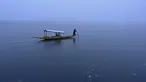 Seorang pria mengendarai perahu di dekat bagian beku danau Dal setelah hujan salju lebat di Srinagar (16/1/2020). Banyak daerah terpencil di lembah telah terputus akibat hujan salju lebat tersebut. (AFP Photo/Tauseef Mustafa)