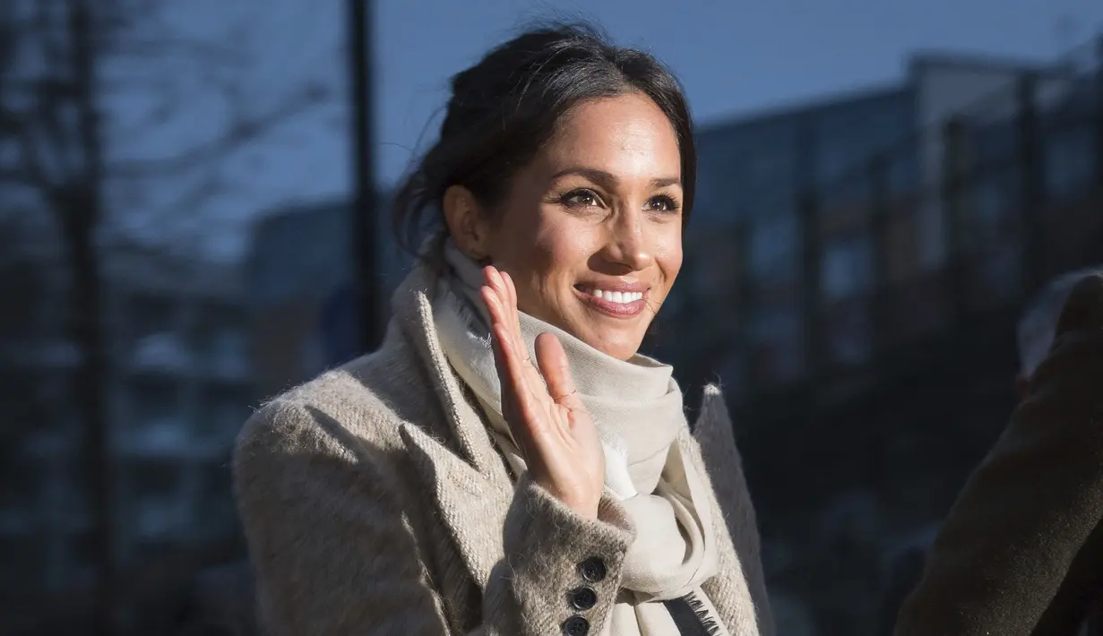 Meghan Markle tersenyum sambil melambaikan tangan kepada warga saat ikut kunjungan Pangeran Harry ke stasiun radio Reprezent 107,3 FM di Brixton, London, Selasa, (9/1). (AP Photo/Dominic Lipinski, Pool)